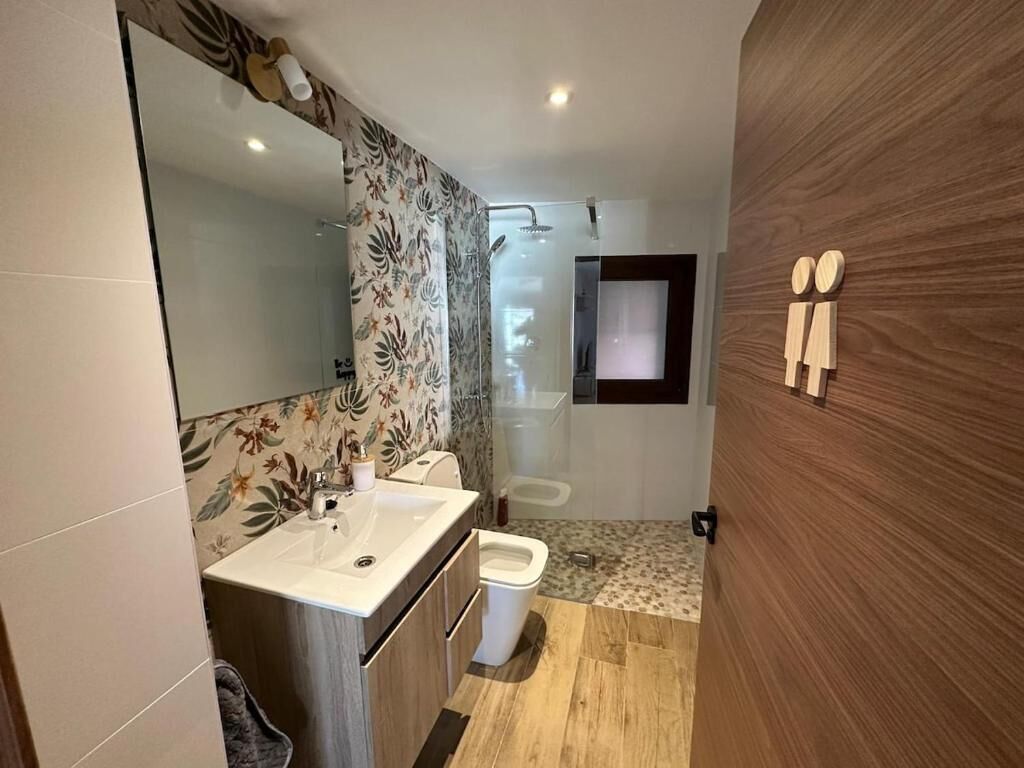Un baño moderno con un espejo grande, lavamanos, inodoro y zona de ducha.