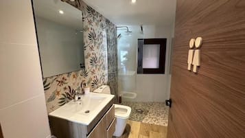 Un baño moderno con un espejo grande, lavamanos, inodoro y zona de ducha.