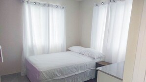 Una camera da letto con un letto, un comodino, una cassettiera e una finestra con tende.