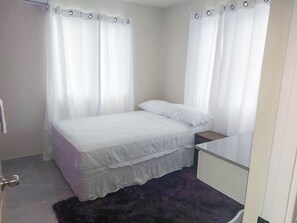 A bedroom with a bed, a nightstand, a dresser, and a window with curtains.