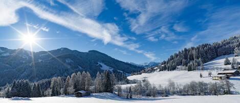 A snow-covered landscape with mountains, a clear sky, and a small cabin.