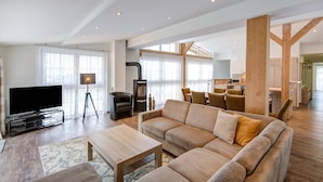 A spacious living room with a large sofa, a coffee table, and a flat-screen TV. There is a dining area with chairs and a kitchen in the background. - Wildschonau Ski-in Brunner Apartment (Wildschönau)