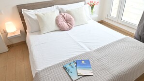 Een net opgemaakt bed met een gewatteerde sprei, een roze kussen en twee boeken op het bed.