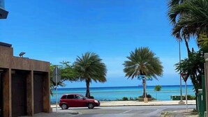 Un coche rojo aparcado en una calle con vistas al océano y palmeras.