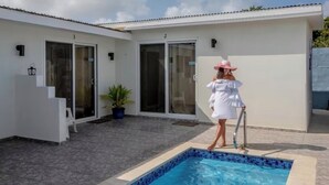 Un área de piscina con suelo de baldosas, una piscina con azulejos azules y una persona vestida de blanco y con un sombrero rosa.