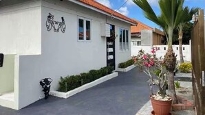 Un bâtiment d’un seul étage, avec un toit recouvert de tuiles, un symbole de vélo peint sur le mur et un pot de fleurs en premier plan.