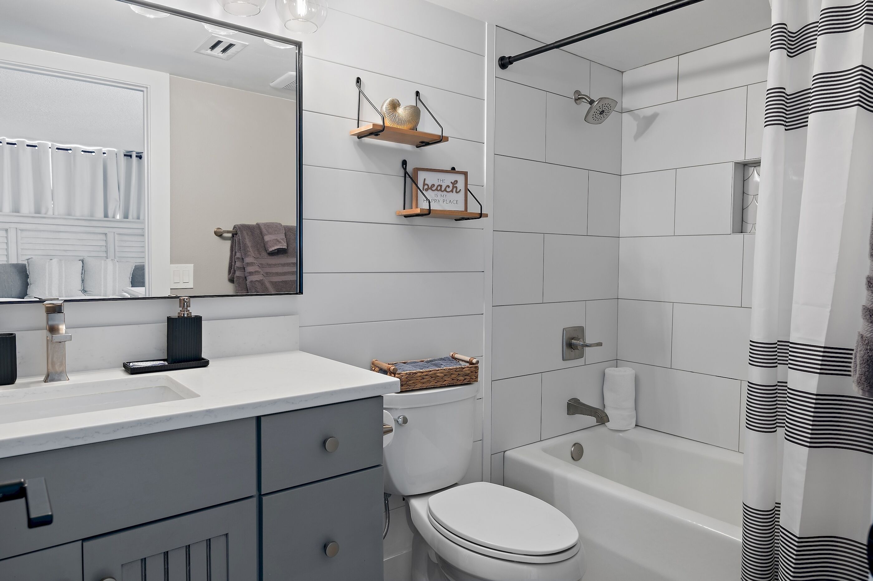 A bathroom with a white sink, toilet, and bathtub. There are two shelves with decorative items and a towel rack.