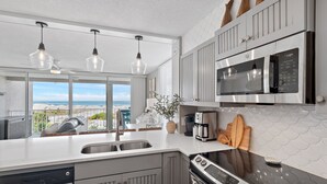 Cozinha moderna com uma ilha grande, eletrodomésticos de aço inoxidável e vista para a praia.