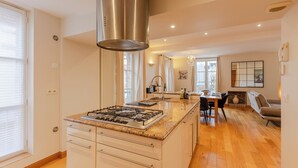 A modern kitchen with a central island, stainless steel range hood, and a dining area with a chandelier.