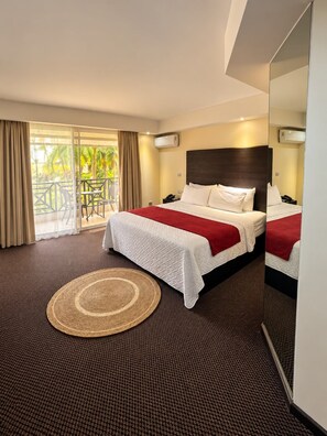 A hotel room with a bed, a round woven rug, a balcony with a view of palm trees, and a large mirror. - Hotel Niza Garden Suites (Las Terrenas)