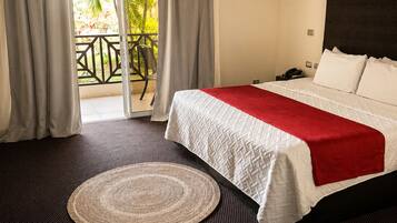 Une chambre d’hôtel avec un lit, un tapis rond en fibres naturelles, un balcon avec vue sur les palmiers et un appareil de climatisation.