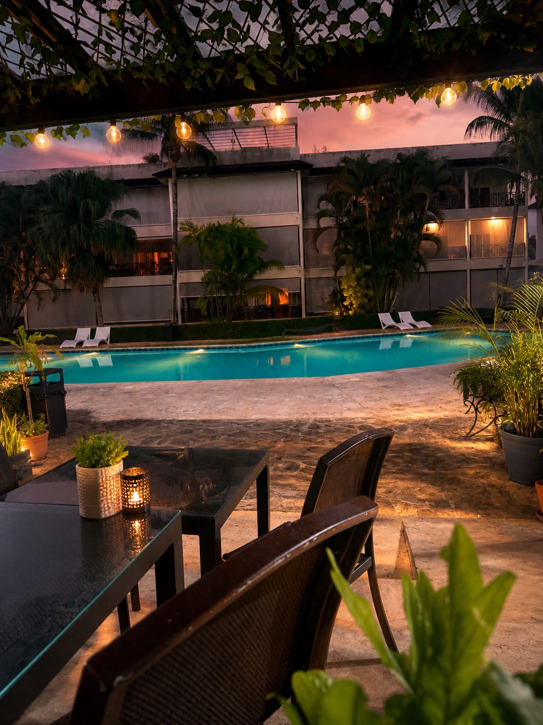 Zona de piscina exterior amb gandules, taula i cadires, i plantes en testos.