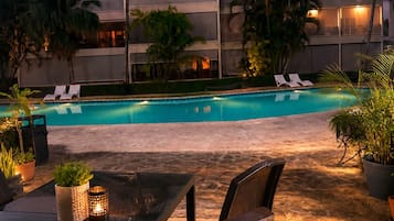 Un área de piscina al aire libre con sillones de descanso, una mesa con sillas y plantas en macetas.
