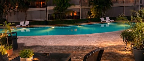 An outdoor pool area with lounge chairs, a table with chairs, and potted plants.