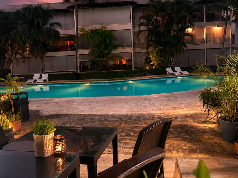 Un área de piscina al aire libre con sillones de descanso, una mesa con sillas y plantas en macetas.