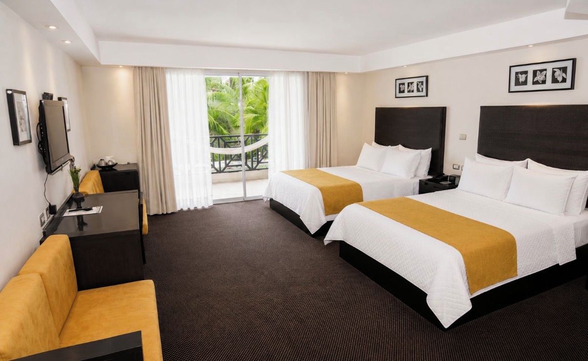 A hotel room with two beds, a desk, a chair, and a TV.