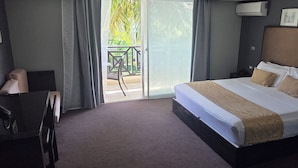 Une chambre d’hôtel avec un grand lit, un bureau et une vue sur un balcon aménagé avec du mobilier d’extérieur.
