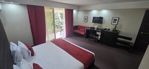 A hotel room with a bed, a desk, a chair, a sofa, and a TV.