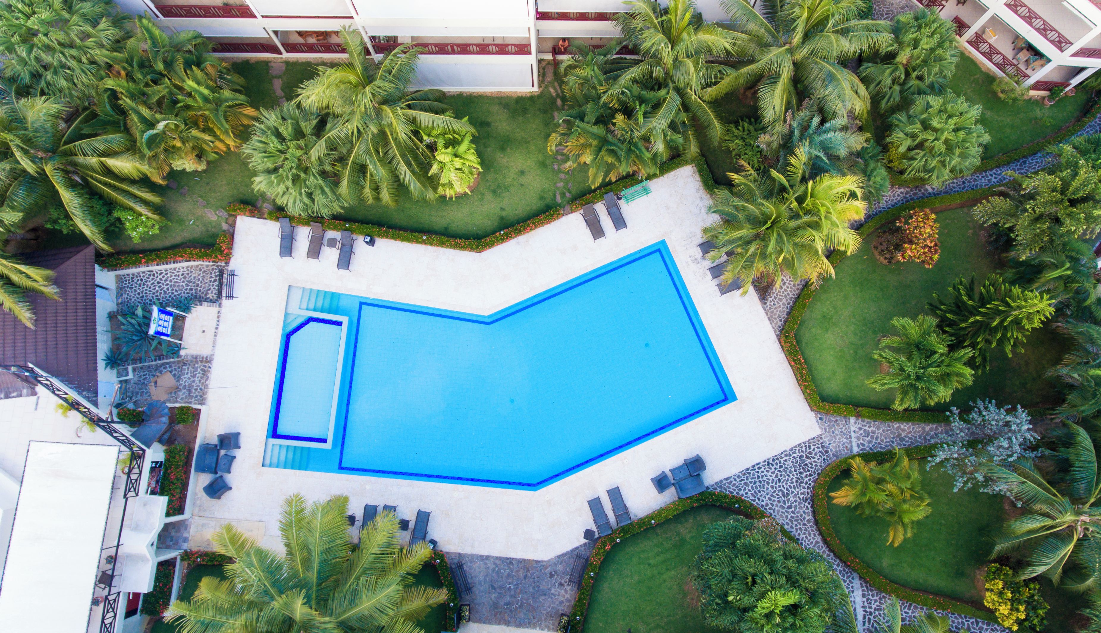 Une vue aérienne d’une piscine entourée de palmiers et d’un bâtiment blanc.