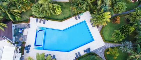 An aerial view of a swimming pool surrounded by palm trees and a white building.