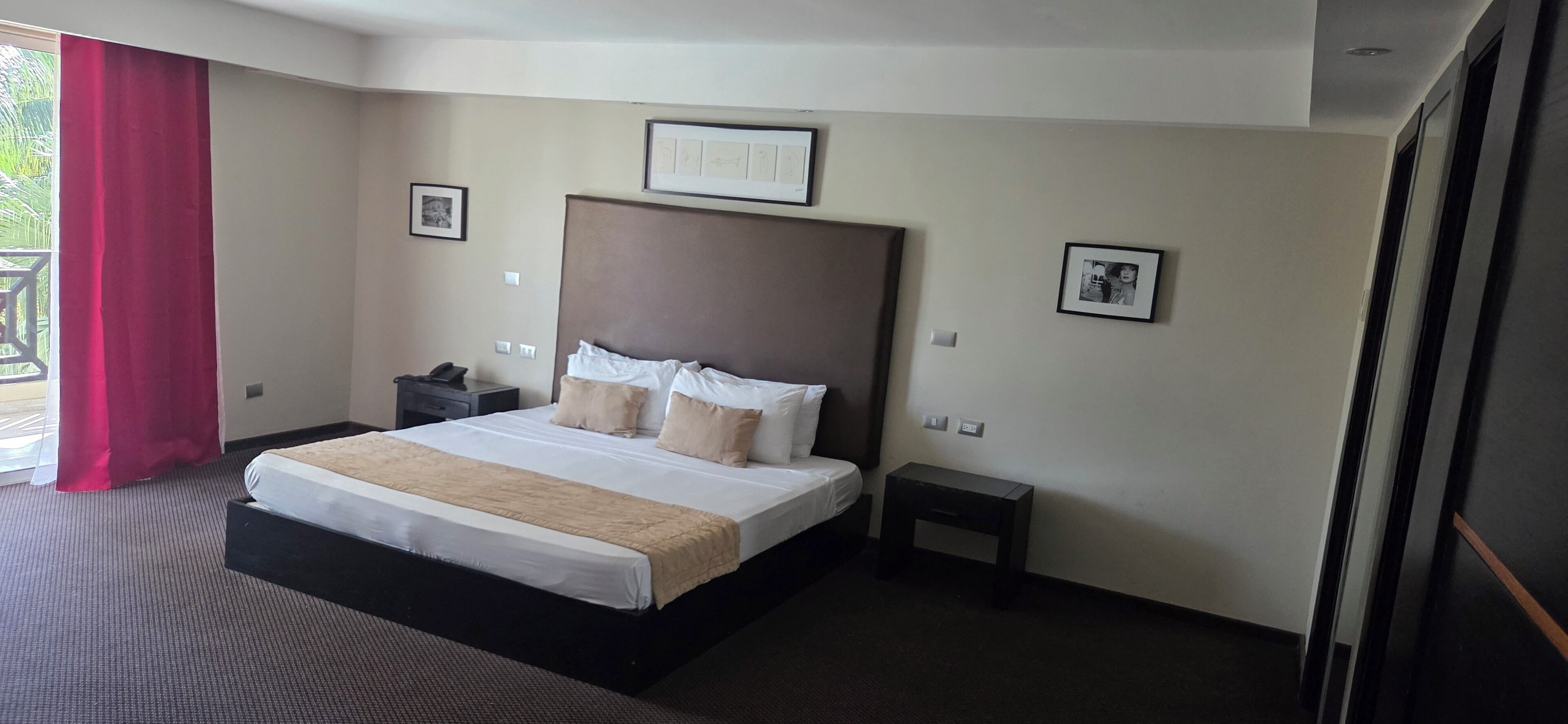 Ein Hotelzimmer mit einem großen Bett, einem Nachttisch, einem Beistelltisch und einem Fenster mit rotem Vorhang.