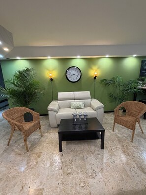 Una sala de estar con un sofá, dos sillones de mimbre, una mesa de centro y un reloj de pared.