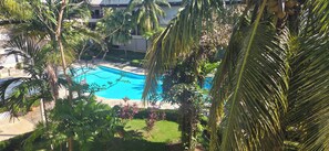 A swimming pool surrounded by palm trees and greenery, with a building in the background.