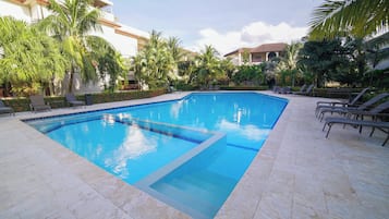 Una piscina con agua azul cristalina, rodeada de sillas de descanso y palmeras.