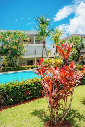 A pool area with a clear sky, palm trees, and a building with balconies.