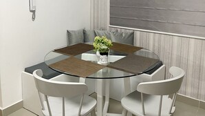 Een moderne eetruimte met een glazen tafel omringd door witte stoelen, een potplant en een bord met de tekst 