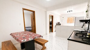 Ein kleines Zimmer mit einem Bett, einem Tisch, einer Bank, einer Küchenzeile und einem Badezimmer.
