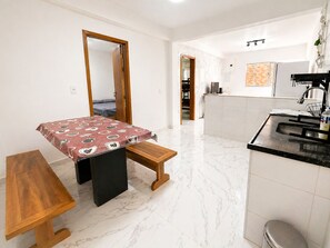 Une pièce de taille modeste comprenant un lit, une petite table, un banc, un coin cuisine et une salle de bain.