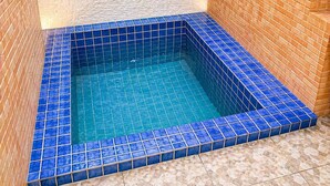 Ein quadratisches Whirlpoolbecken mit blauen Fliesen, umgeben von beige- und braunen Fliesen.