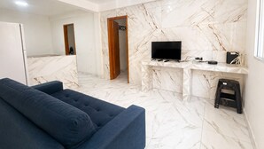 Ein modernes Wohnzimmer mit einem dunkelblauen Sofa, einem Flachbildfernseher an einer Marmorwand und einem kleinen Hocker.