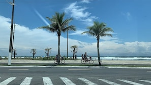 Eine Küstenstraße mit Palmen, einem Strand und Radfahrern.