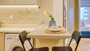 Une cuisine compacte équipée d’un lave-linge, d’une table à manger avec des chaises et d’une petite fenêtre.