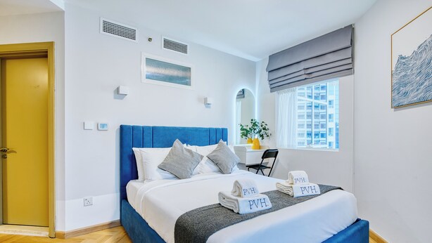 Une chambre d’hôtel moderne, dotée d’un grand lit, d’un bureau et d’une fenêtre donnant sur des immeubles.