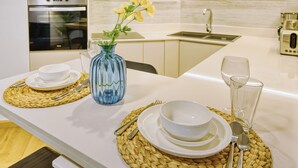Une cuisine moderne équipée d’un four à micro-ondes, d’un four et d’un évier. On y trouve deux sets de table en fibres naturelles, un vase avec des fleurs et un verre d’eau sur le comptoir.