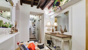 A hallway with a mirror, decorative items, a wicker basket with various objects, and a small table with a lamp and a glass. - PIAZZA NAVONA ADORABLE APARTMENT (Roma)