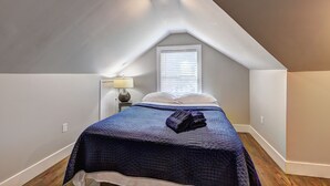A bedroom with a sloped ceiling, a bed with a blue quilt, a bedside lamp, and a window with blinds. - Spacious 4-bedroom house in tranquil Decatur with AC (Decatur)