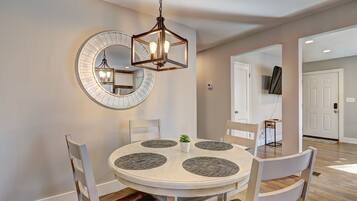 Un coin repas comprenant une table ronde, quatre chaises, un luminaire suspendu et un grand miroir au mur.