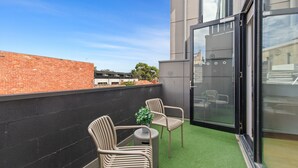A balcony with two chairs and a small table, a potted plant, and a glass door leading to an interior space. - Lovely 1-bed With Balcony in St Kilda's Heart (Melbourne)