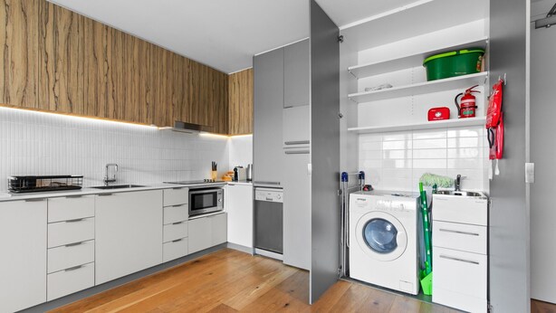 A modern kitchen with white cabinetry, a built-in oven, a dishwasher, and a washing machine. - Lovely 1-bed With Balcony in St Kilda's Heart (Melbourne)