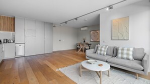 A modern kitchen with white cabinets and a wooden floor, a grey sofa with checkered cushions, and a round coffee table. - Lovely 1-bed With Balcony in St Kilda's Heart (Melbourne)