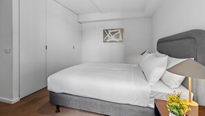 A bedroom with a bed, a nightstand, a lamp, and a wall-mounted artwork. - Lovely 1-bed With Balcony in St Kilda's Heart (Melbourne)