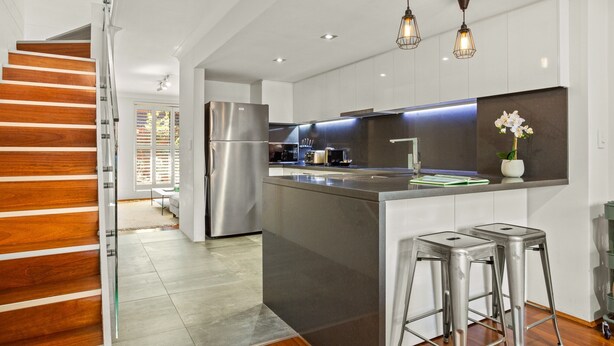 Una cocina moderna con un refrigerador de acero inoxidable, una isla central con taburetes e iluminación colgante.