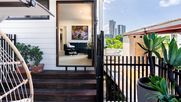 Una casa moderna con un portón negro, una escalera de madera y vistas a un paisaje urbano.