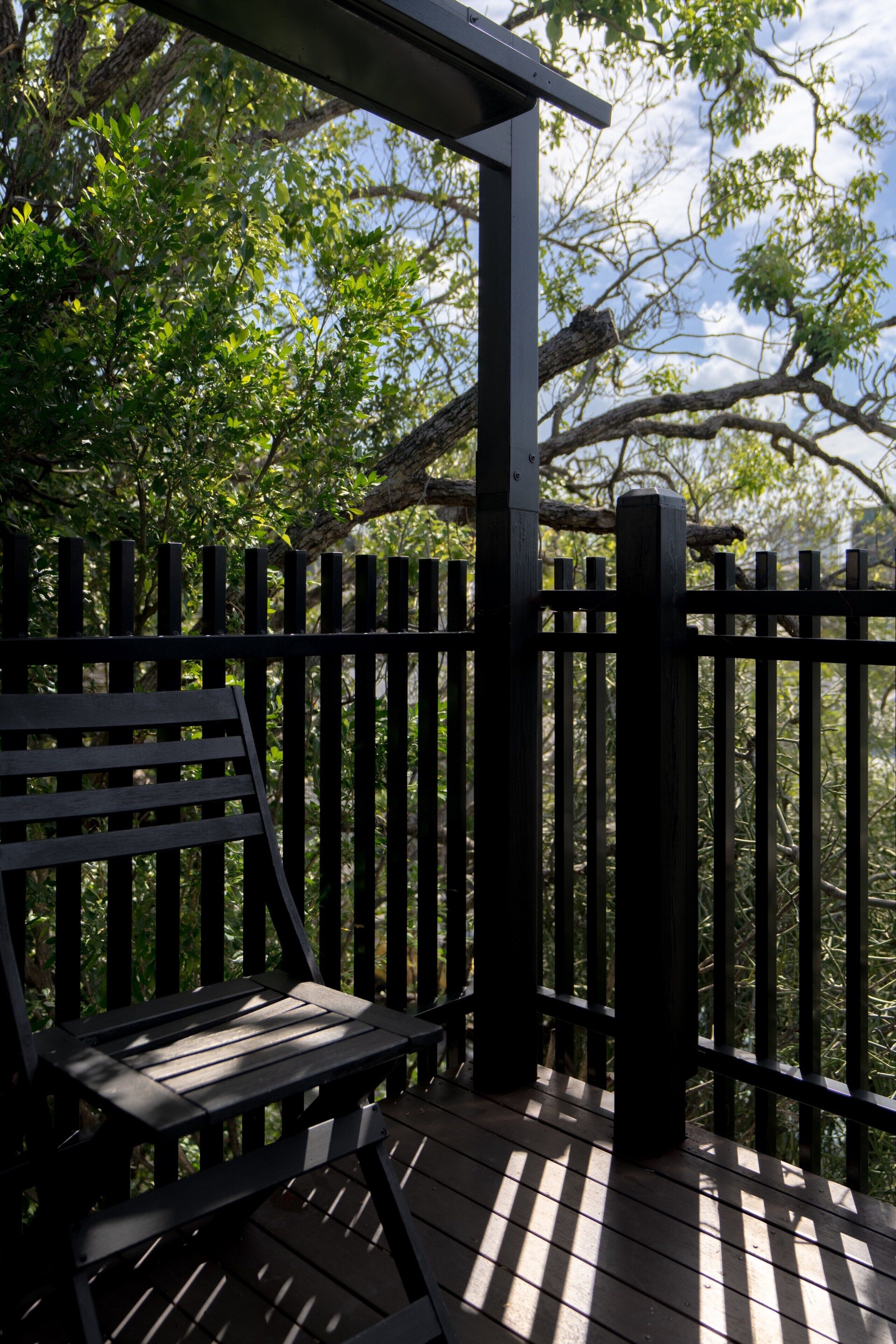 A wooden deck with a bench, surrounded by a black metal fence, overlooking a lush green landscape.