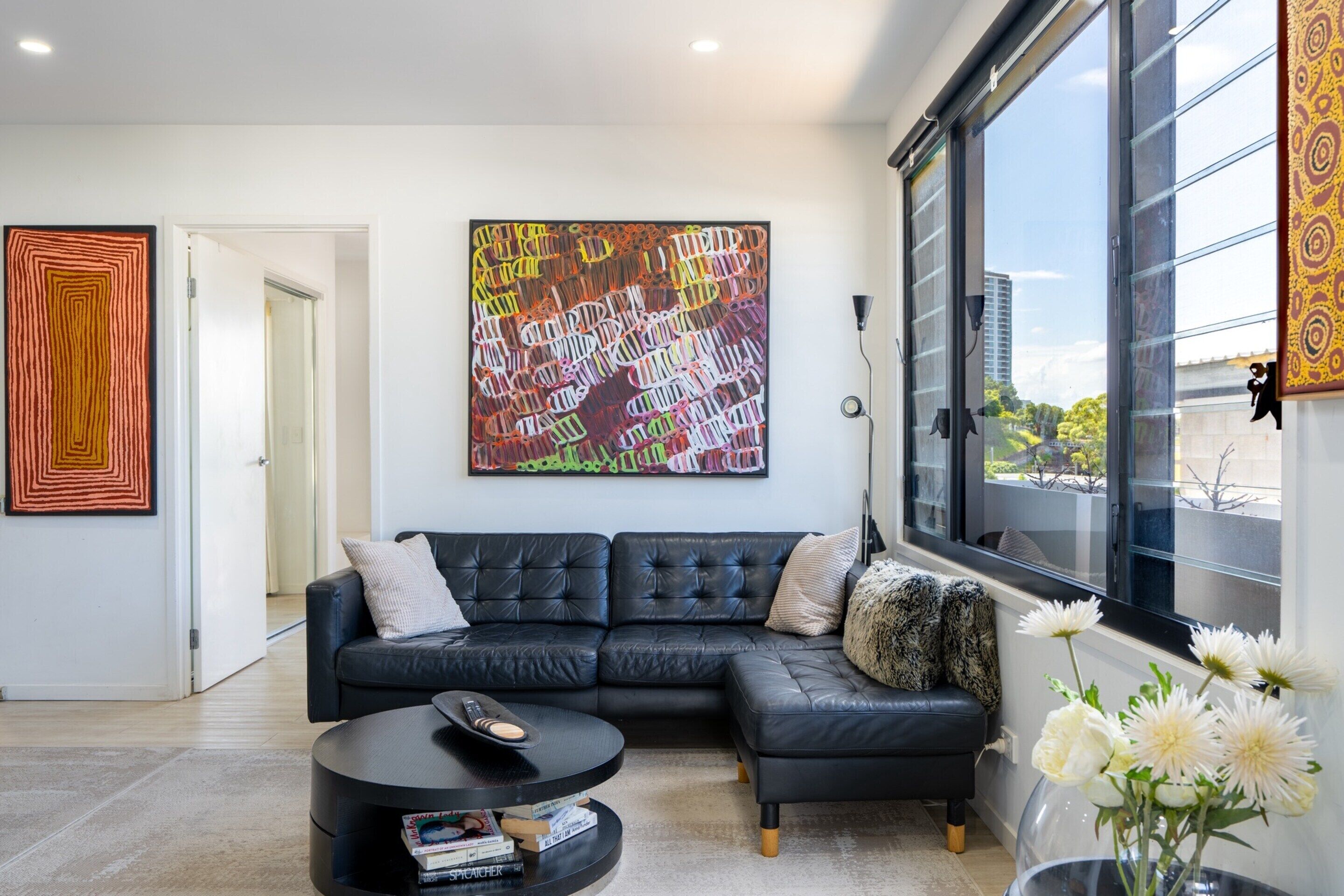 A modern living room with a black leather sofa, a round coffee table, and a large abstract painting on the wall.