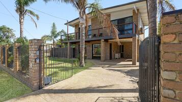 A two-story house with a balcony, a gated entrance, and a paved driveway.